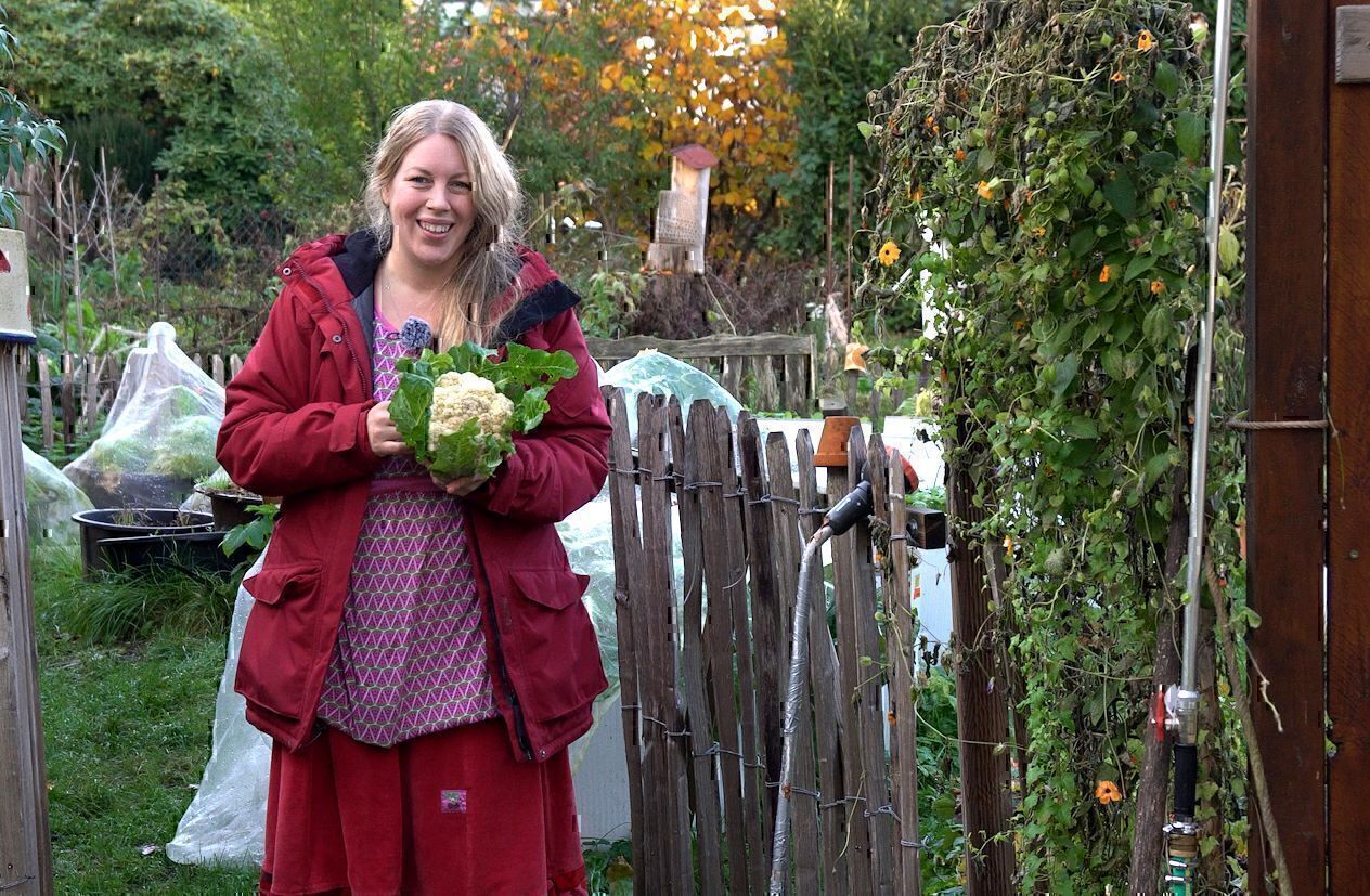 Jen in roter Jacke hält im Herbstgarten einen Blumenkohlkopf mit Blättern