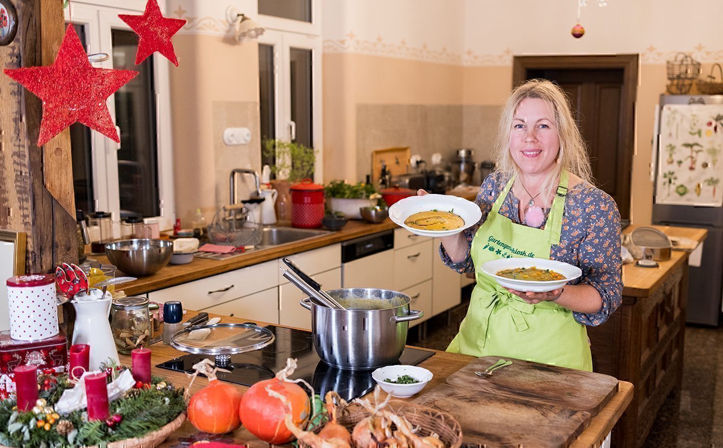 Jen steht in der Küche und hält zwei Teller Kürbissuppe, davor liegen Hokkaido-Kürbisse